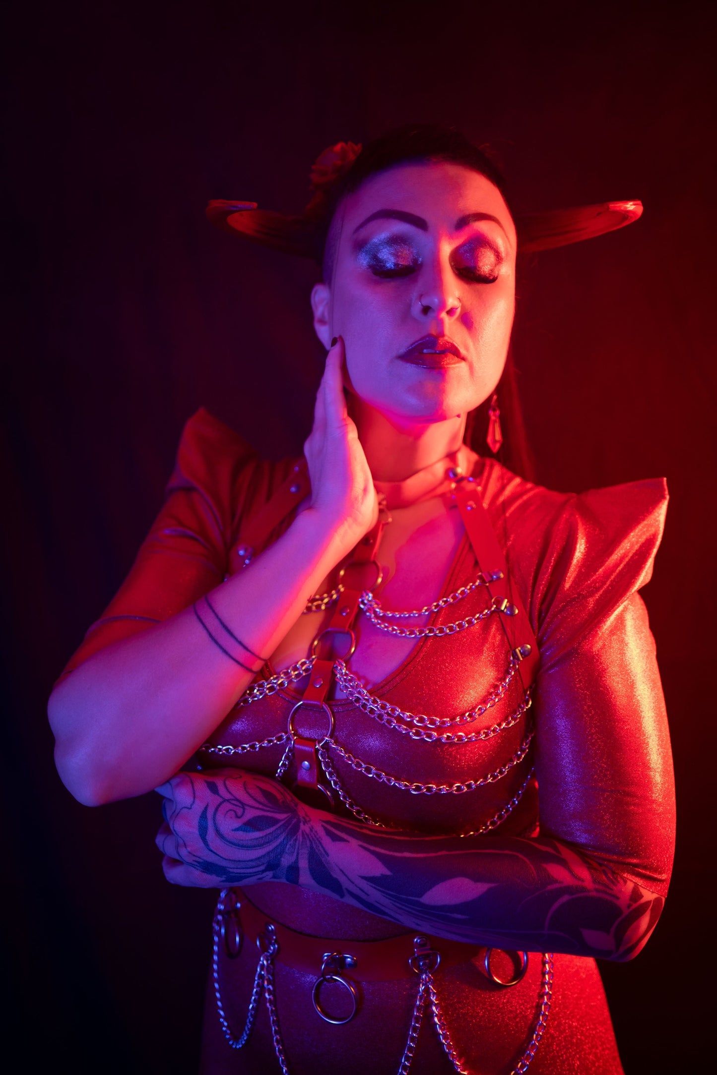 Zoe Sol models Azazel horns by Haus of Brimstone in a glossy red ensemble with harness and chains. Photo by Optic Onslaught.
