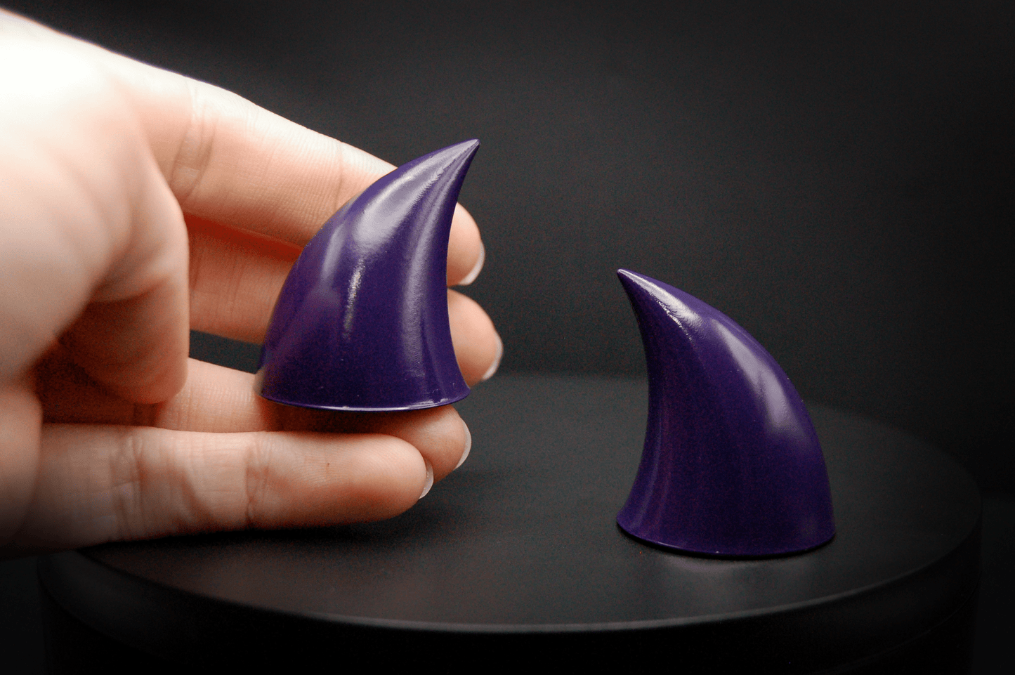 A hand holding an imp devil horn in belladonna violet, a dark purple with a glossy finish.