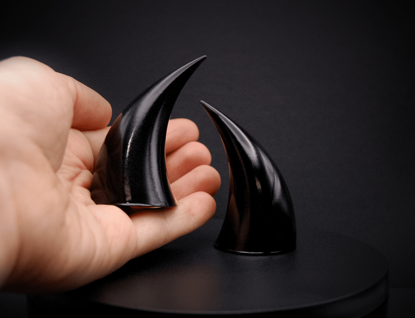 A hand holding an incubus devil horn in black with a glossy finish.