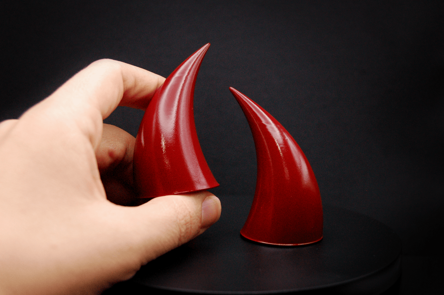 A hand holding an incubus devil horn in bordeaux red with a glossy finish.