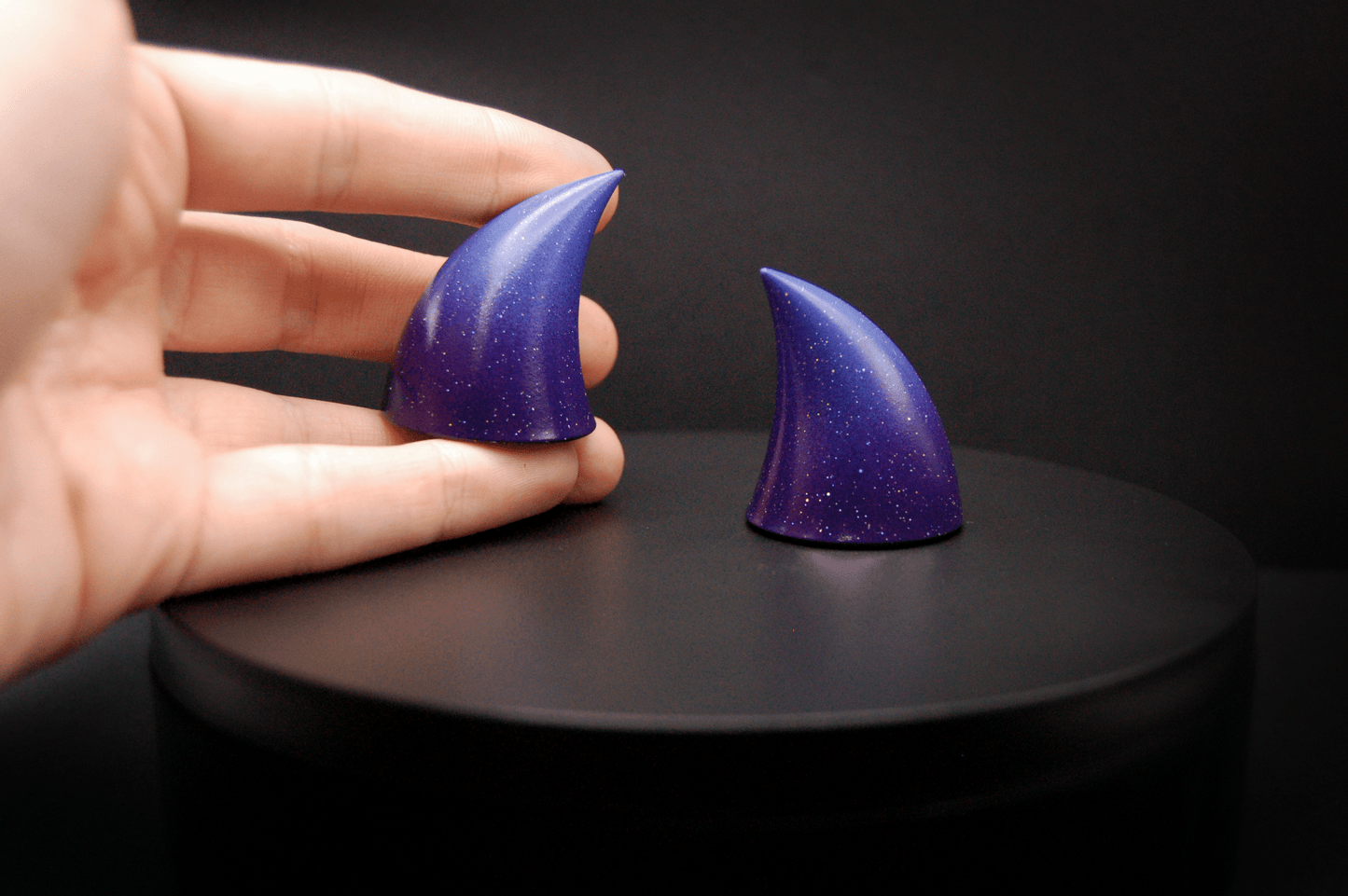 Hand holding an imp devil horn in a royal purple to periwinkle ombré with a glittery finish.