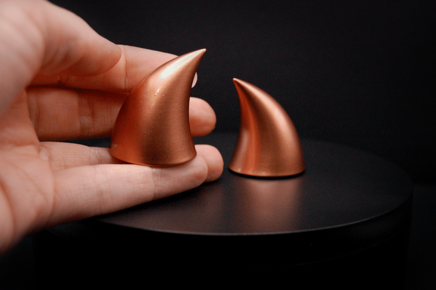 A hand holding an imp devil horn in metallic copper.