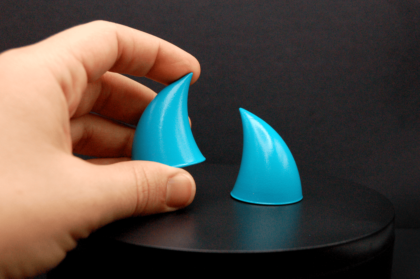 A hand holding an imp devil horn in naiad blue, a cyan color with a glossy finish.