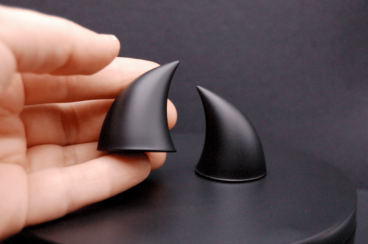 A hand holding an imp devil horn in black with a matte finish.