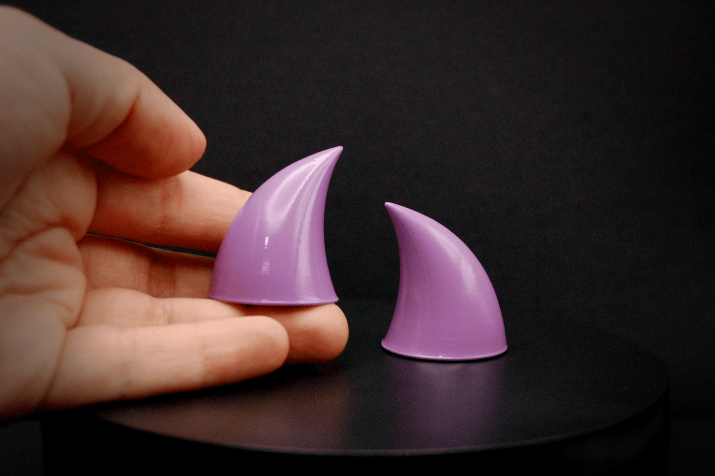 A hand holding an imp devil horn in lilac with a glossy finish.