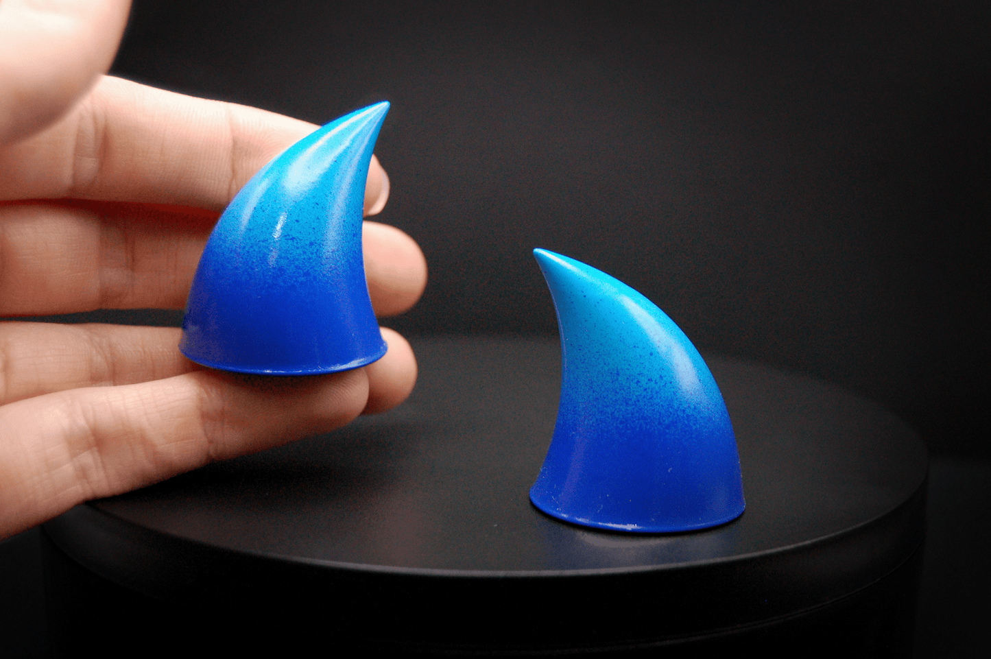 A hand holding an imp devil horn in a royal blue to sky blue ombré with a glossy finish.
