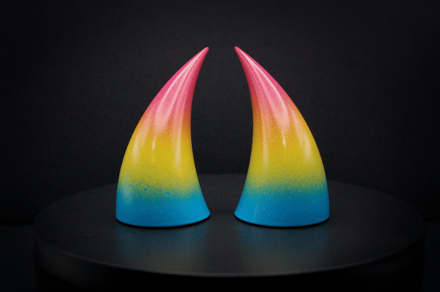 Front view of imp devil horns in a sky blue, to bright yellow, to warm pink ombré, the colors of the pansexual pride flag with a glittery finish.