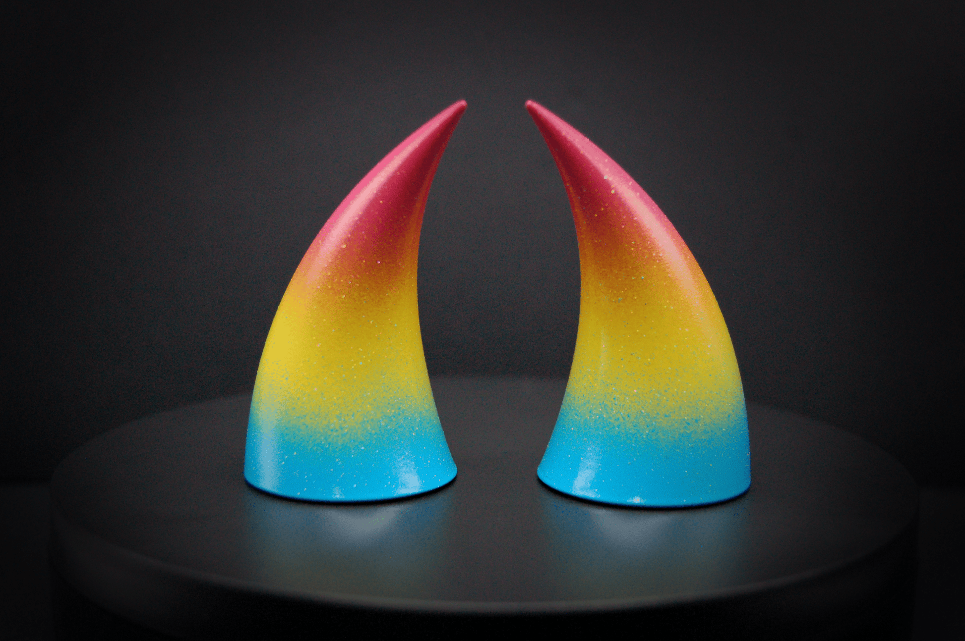 Back view of imp devil horns in a  sky blue, to bright yellow, to warm pink ombré, the colors of the pansexual pride flag  with a glittery finish.