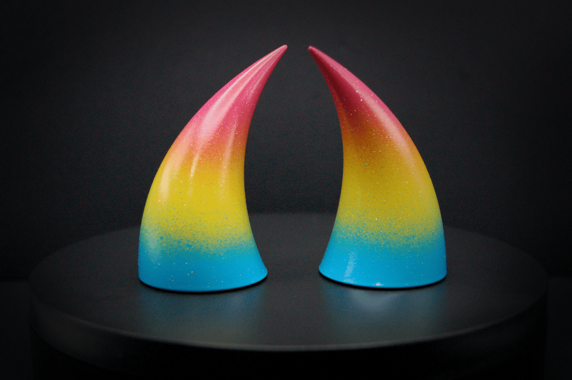 Side view of imp devil horns in a sky blue, to bright yellow, to warm pink ombré, the colors of the pansexual pride flag  with a glittery finish.