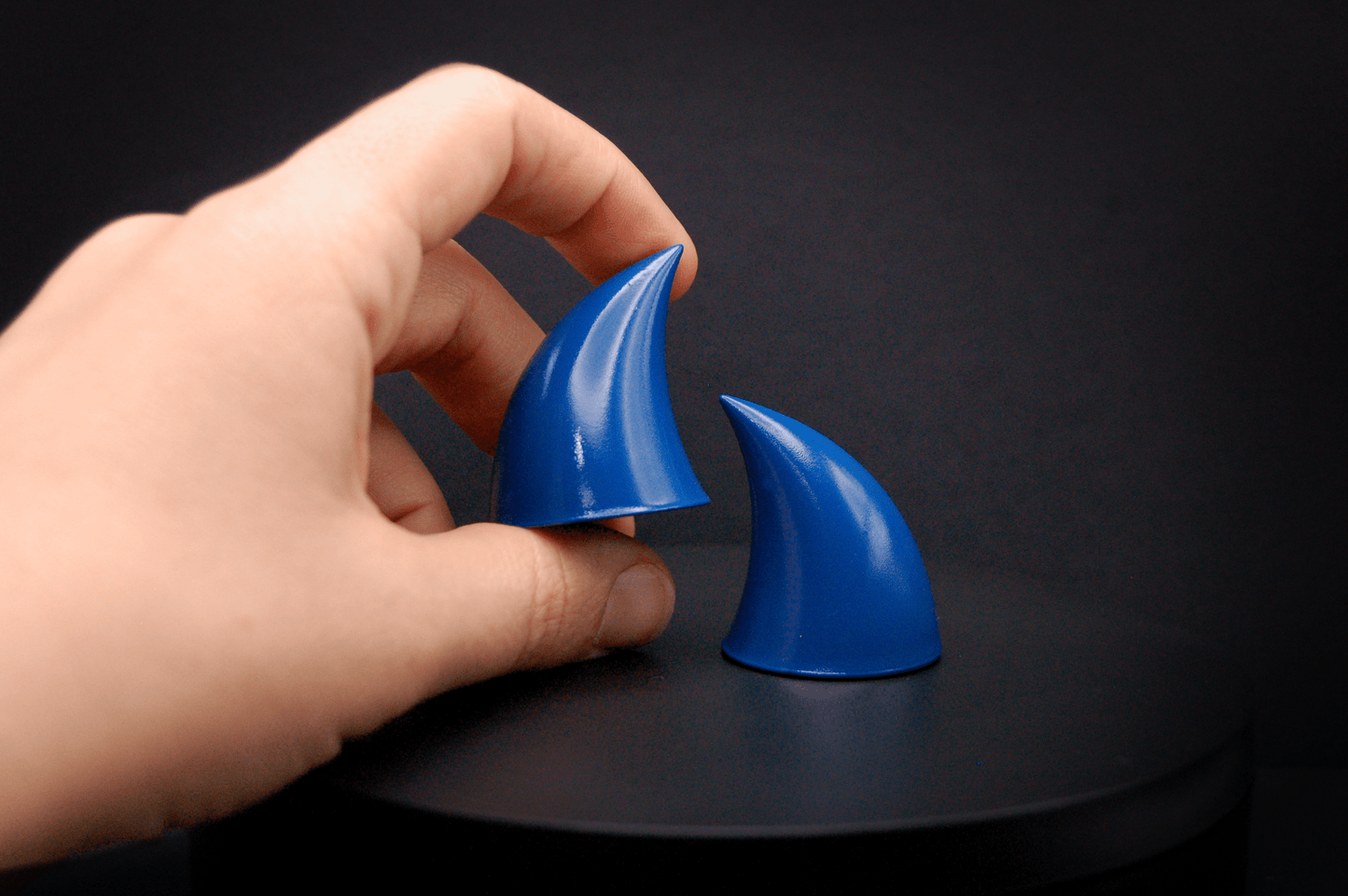 A hand holding an imp devil horn in storm blue, a deep blue with a glossy finish.