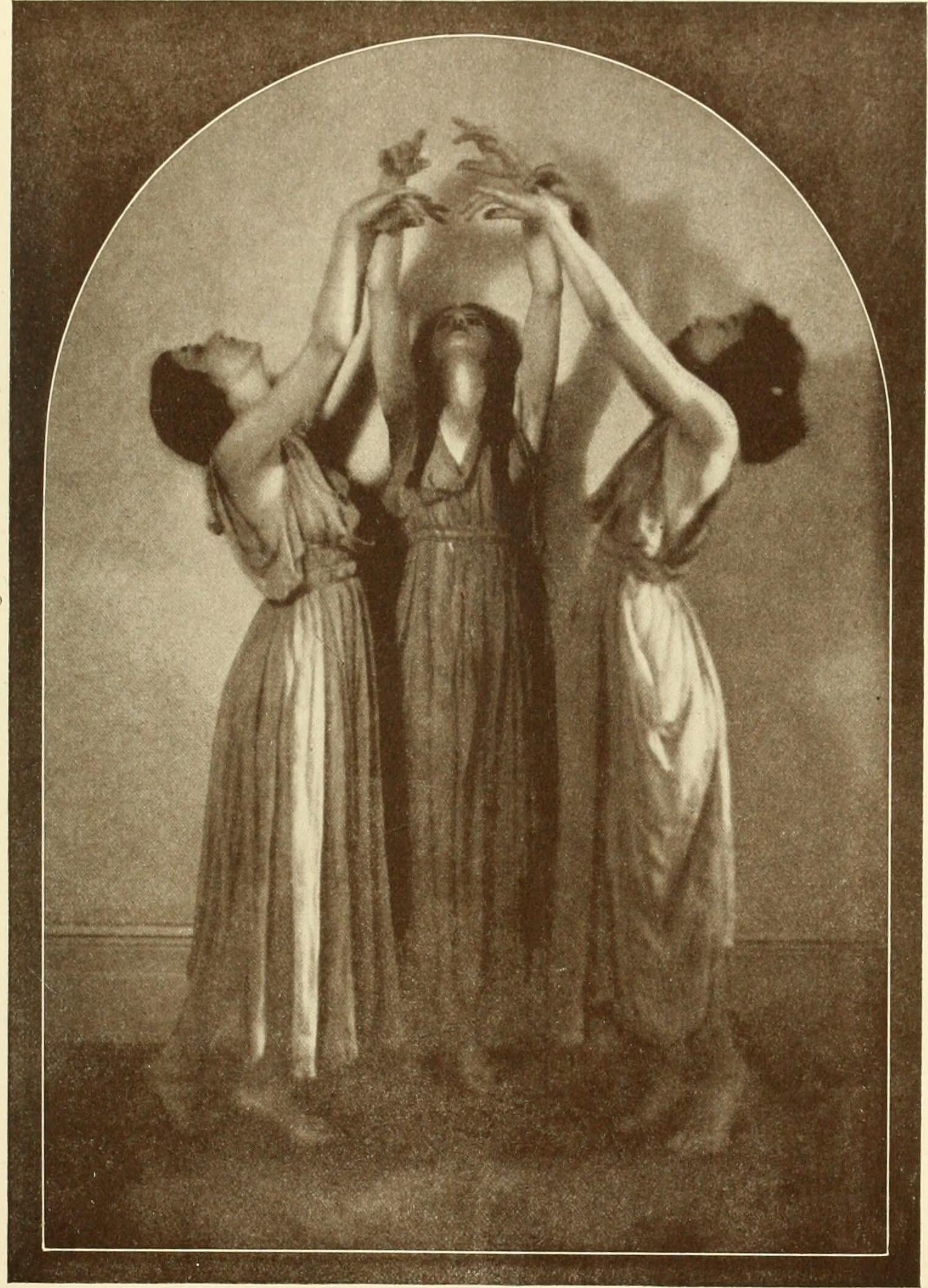 Three women in classical robes facing each other and holding their arms together in the air in a mystical pose.