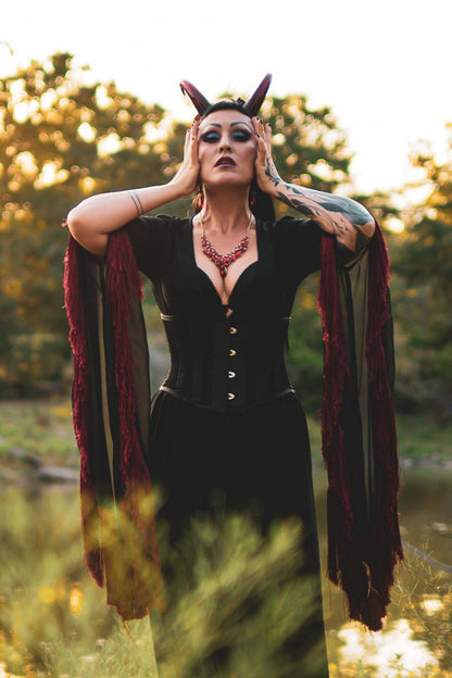 Zoe Sol models Azazel horns by Haus of Brimstone in a black and red witchy ensemble, their hands at the side of their face, in a field at golden hour. Photo by Optic Onslaught.