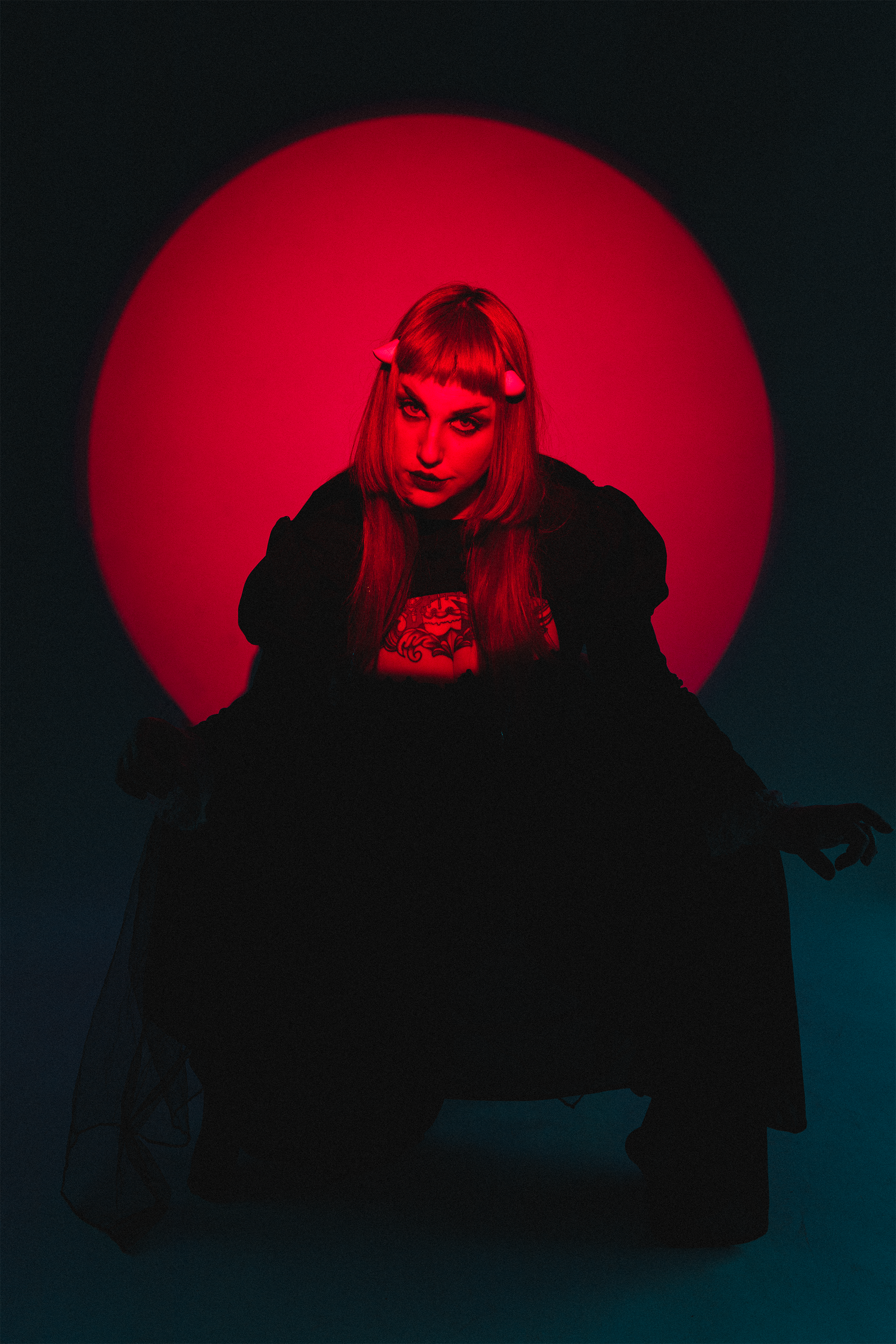 Model Stormy September poses in a red spotlight in gothic attire wearing imp horns under her bangs. Photo by Matt Stone.