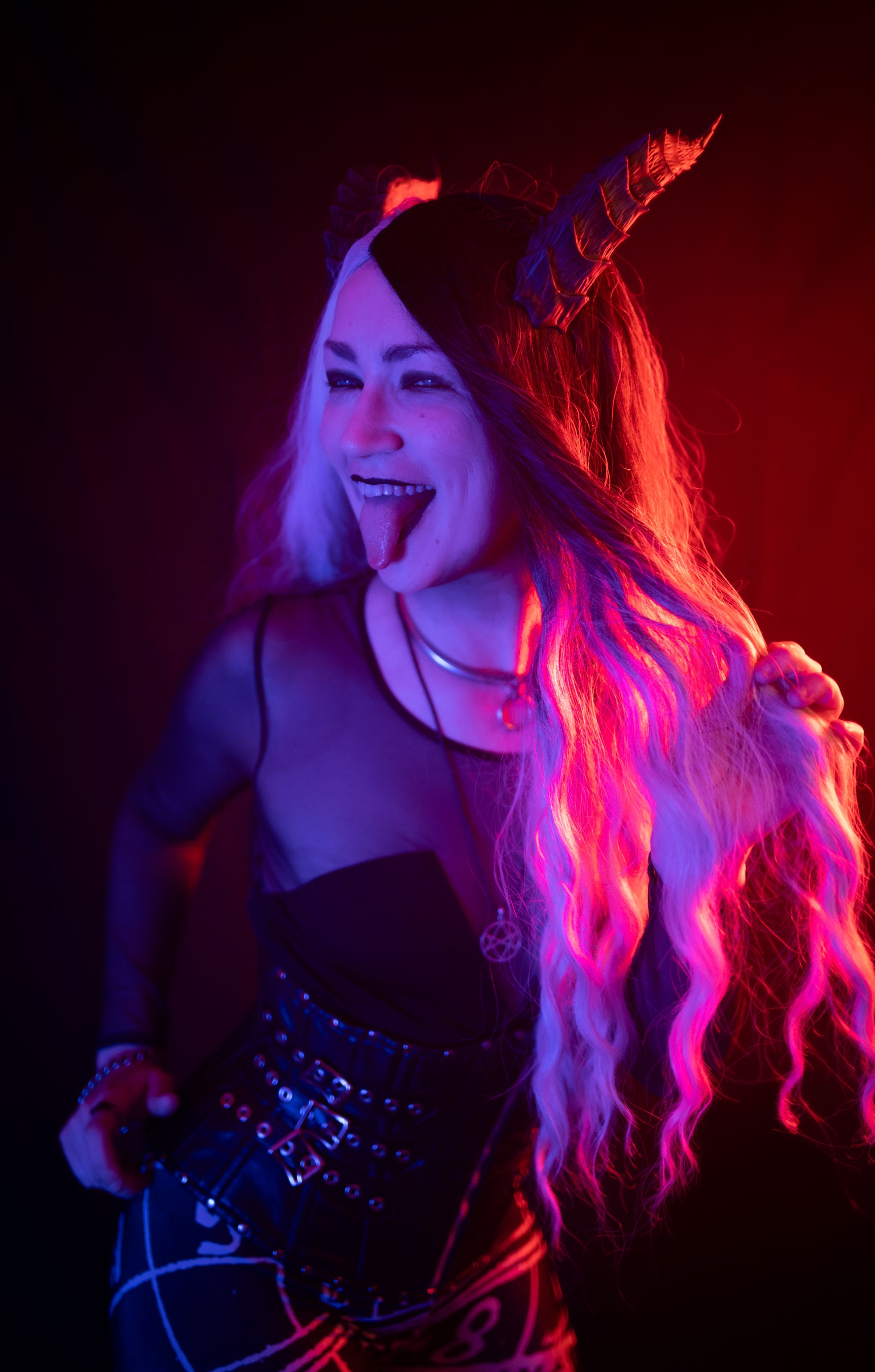 Sabor Insanity sticks out their tongue while modeling black Tiefling horns by Haus of Brimstone in witchy gothic attire. Photo by Optic Onslaught.
