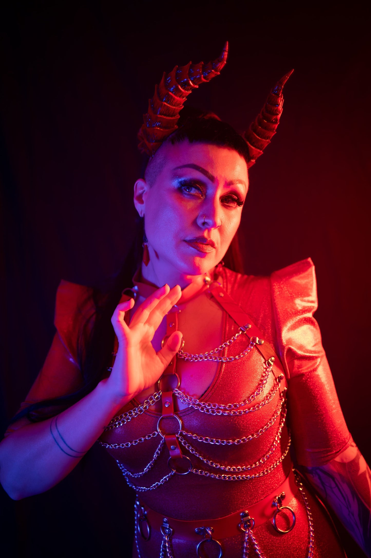 Zoe Sol models scarlet Tiefling horns by Haus of Brimstone in a glossy red ensemble with harness and chains. Photo by Optic Onslaught.
