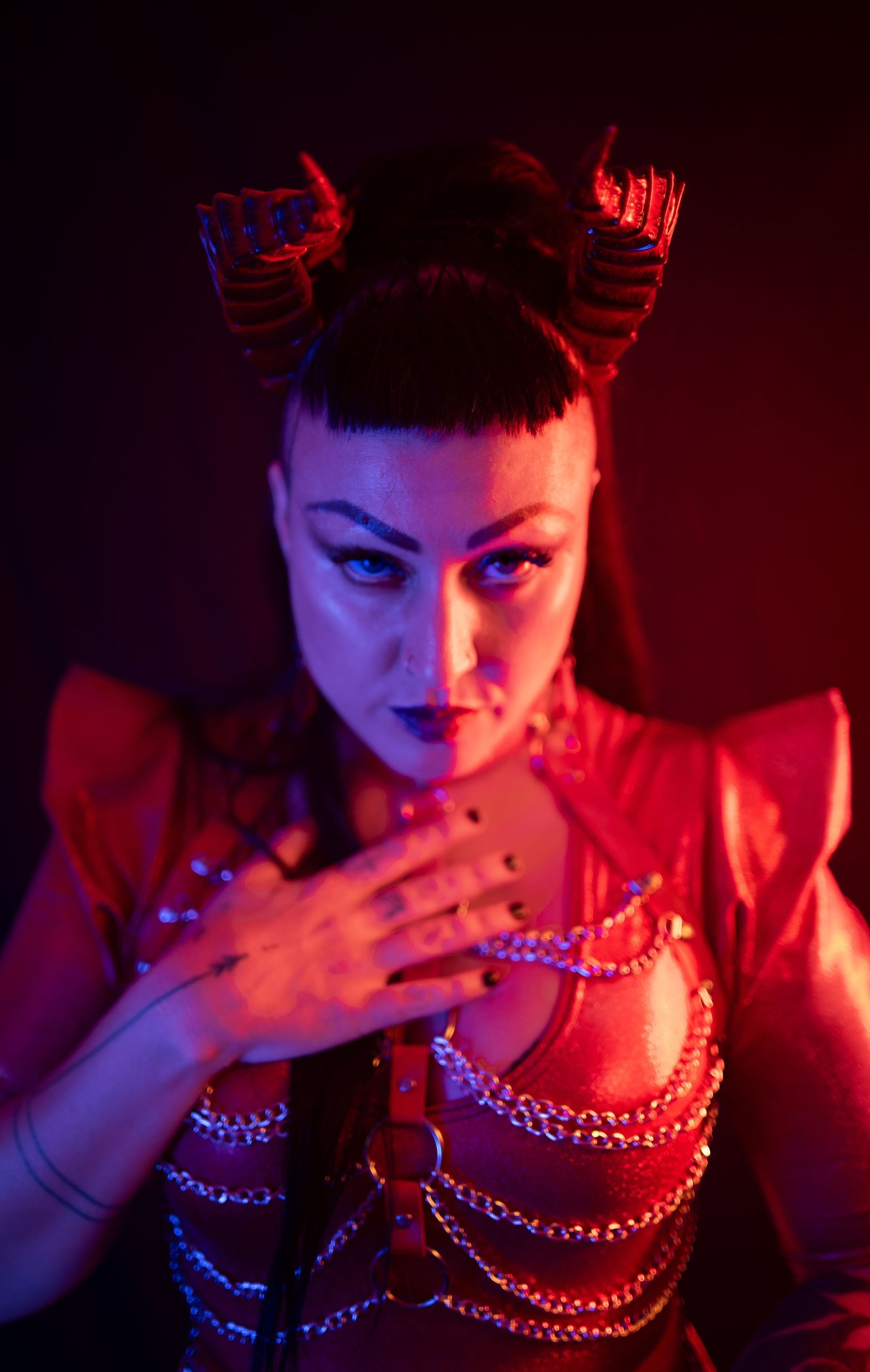 Zoe Sol models scarlet Tiefling horns by Haus of Brimstone in a glossy red ensemble with harness and chains. Photo by Optic Onslaught.