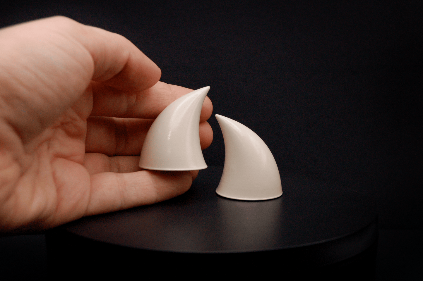 Hand holding an imp devil horn in bone white with a glossy finish.
