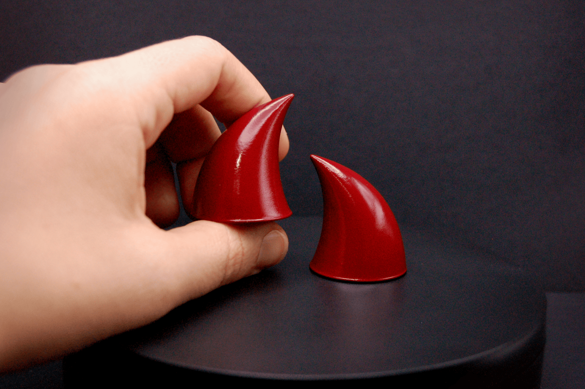 A hand holding an imp devil horn in bordeaux red with a glossy finish.