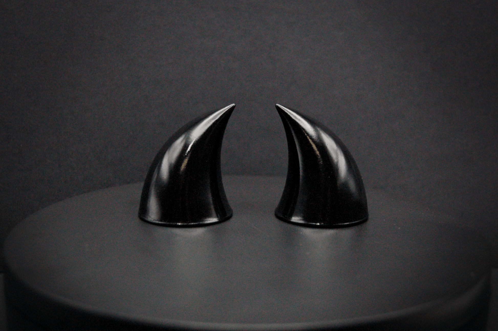 A pair of small black devil horns with a glossy finish.