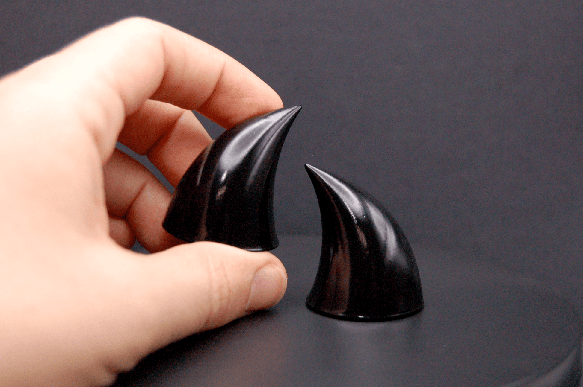 A hand holding an imp devil horn in black with a glossy finish.