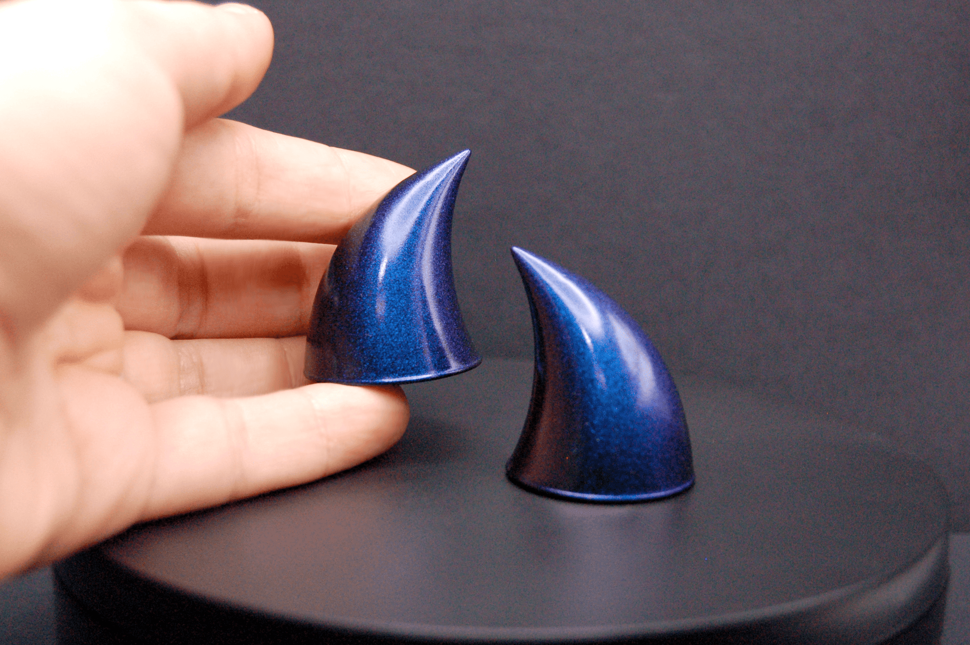 A hand holding an imp devil horn in metallic violet-blue.