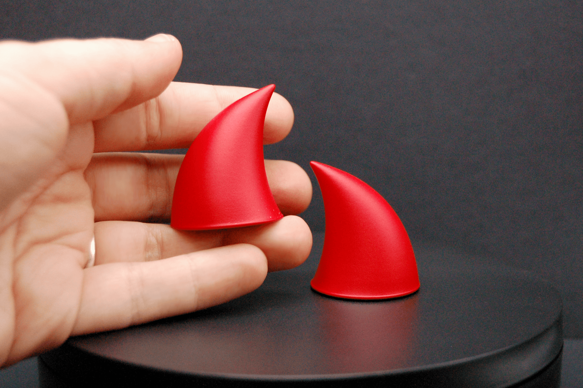 A hand holding an imp devil horn in scarlet red with a matte finish.