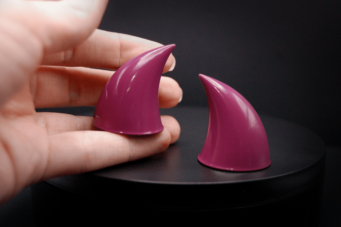 A hand holding an imp devil horn in deep rose  with a glossy finish.