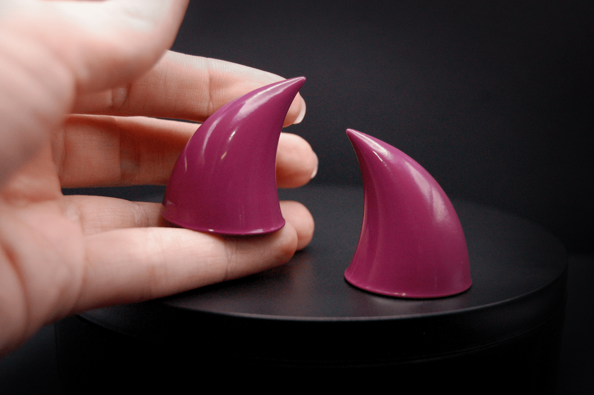 A hand holding an imp devil horn in deep rose  with a glossy finish.